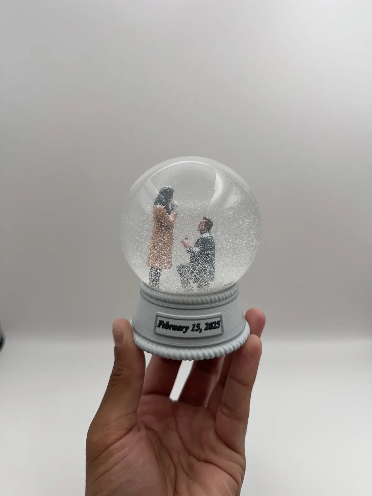 A custom snow globe showing a 3D printed proposal scene on a dated base